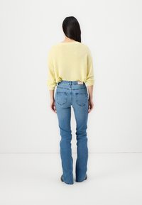 Yellow knit sweater with long sleeves, paired with high-waisted blue jeans featuring a slim fit and flared bottom.