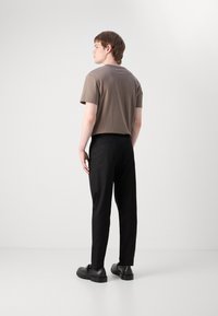 Brun bomulls t-skjorte, korte ermer, kombinert med svarte bukser og svarte sko. Enkel baklomme på buksene, minimalistisk design, glatt tekstur.