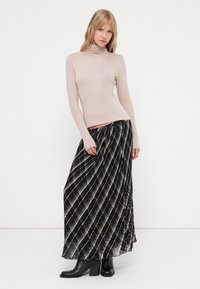 Beżowy sweter z golfem w połączeniu z czarną, plisowaną spódnicą maxi z białym i szarym wzorem w diament, noszoną z czarnymi botkami na obcasie.