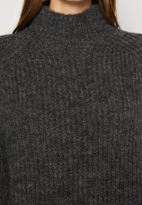 Pull en tricot gris foncé avec un col montant, présentant un motif texturé et côtelé pour la chaleur et le confort.