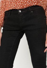 Calças de ganga pretas com um design ajustado, apresentando um fecho frontal por botão, detalhes de costura discretos e bolsos profundos.