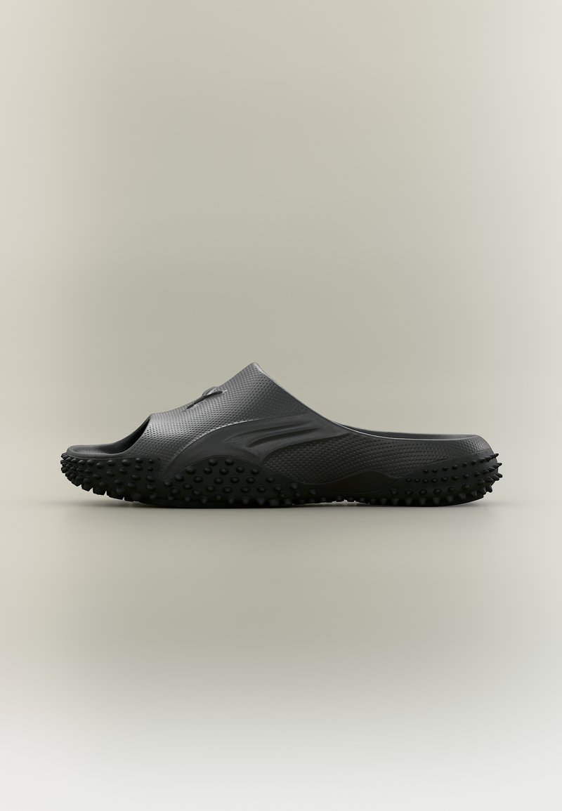 Μαύρο λαστιχένιο σανδάλι χωρίς λουράκι με υφή στη σόλα που διαθέτει μικρές στρογγυλές αντιολισθητικές επιφάνειες, ανοιχτό μπροστινό μέρος και λείο άνω μέρος, με μονόχρωμο φόντο.