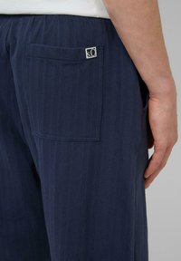 Pantalons bleu marine avec un motif à chevrons texturé, dotés d'une poche arrière et d'une petite étiquette logo. Taille élastique pour un confort optimal.