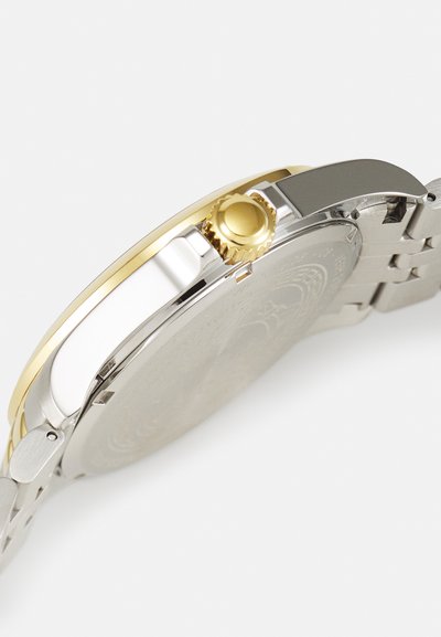 Montre-bracelet argent et or avec un boîtier rond, couronne en métal texturé et bracelet à maillons avec une finition polie.