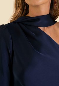 Marineblaue Bluse aus glattem Stoff mit einem drapierten Kragendesign. Verfügt über anliegende Schultern und einen subtilen Glanz. Akzentuiert mit einem teilweisen Kragen.