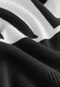 Jersey de punto con un diseño texturizado en blanco y negro, con patrones audaces, tejido suave y un dobladillo acanalado para un detalle adicional.