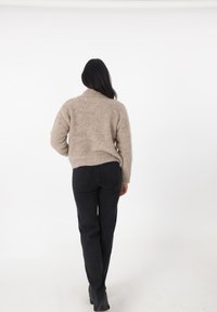 Maglione beige in maglia fuzzy con colletto a risvolto; abbinato a pantaloni neri attillati e stivaletti alla caviglia. Vista posteriore su uno sfondo semplice.