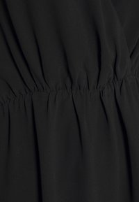 Tissu noir à la texture lisse qui se rassemble à la taille, formant de doux plis. Le design comporte des détails élastiqués pour l'ajustement et la forme.