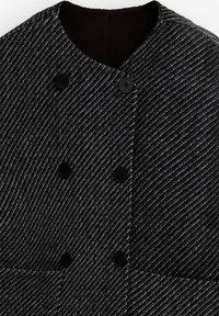 Primo piano di cappotto in lana grigio scuro con strisce diagonali e sei bottoni neri sul davanti, caratterizzato da un colletto rotondo e tessuto strutturato.