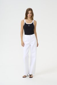 Canotta nera con bordi e logo bianchi, abbinata a pantaloni bianchi a vita alta e a gamba larga. La modella indossa sandali neri con tacco. Texture liscia.