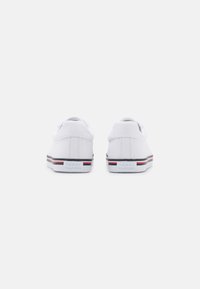 Sneakers bianchi in tela con un design low-top, caratterizzati da un logo sul tallone e accenti a strisce rosse e blu lungo la suola.