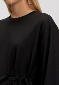 Zwarte lange mouwen shirt van zacht materiaal, met een ontspannen pasvorm en een trekkoorddetail in de taille. Glad textuur en minimalistisch ontwerp.