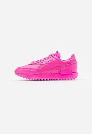 Jaskraworóżowy niski sneaker z teksturowaną podeszwą, frontowym sznurowaniem i markowym paskiem bocznym, pokazany z profilu na białym tle.