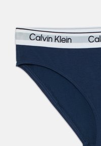 Sötétkék Calvin Klein alsónadrág fehér gumírozott derékkal, fekete logóval és fekete dupla csíkkal a felső szélen.