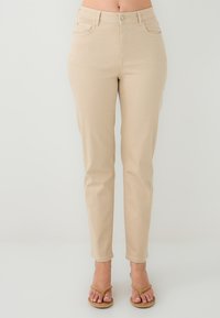 Pantalons slim beige avec une texture lisse, poches avant et fermeture à bouton. Design de jambe fuselée, atteignant le mollet.