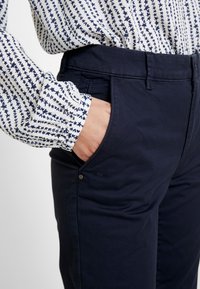 Marynarskie spodnie o gładkiej fakturze, z bocznymi kieszeniami i detalem w postaci guzika. W połączeniu z białą bluzką wzorzystą w granatowe gwiazdy.