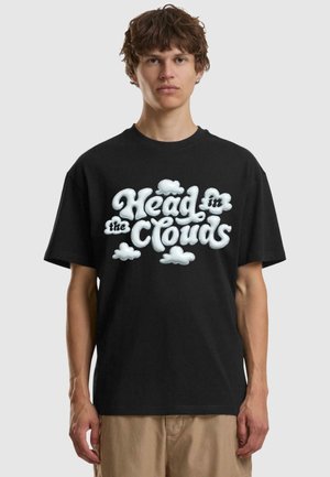 Schwarzes Baumwoll-T-Shirt mit einem großen, weißen, wolkenartigen Grafik, auf der steht "Kopf in den Wolken" in einer verspielten, geschwungenen Schrift.