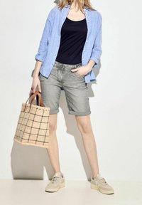 Chemise boutons en bleu clair sur un débardeur noir, shorts en denim gris roulés, baskets beiges et sac fourre-tout à carreaux beige.
