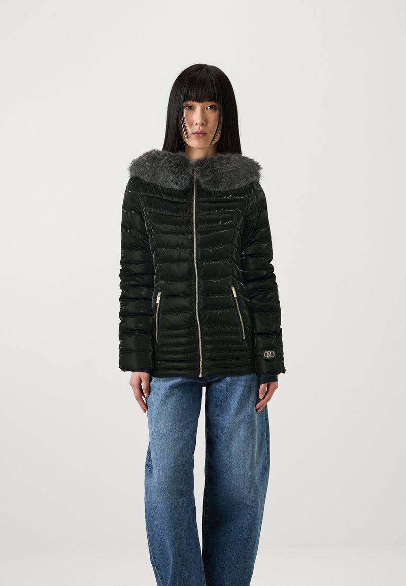 Svart pufferjakke med fuskepelskrage, med gullglidelåser og horisontal søm, kombinert med løstsittende blå jeans.