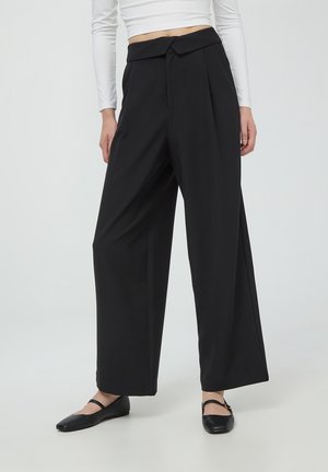 Pantaloni neri a gamba larga in tessuto leggero con frontale plissettato e dettaglio in vita annodato. Abbinati a ballerine nere.