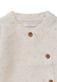 Kremowy sweter w robionym na drutach wzorze, z brązowymi guzikami i subtelnymi pomarańczowymi akcentami. Metka głosi "noppies."