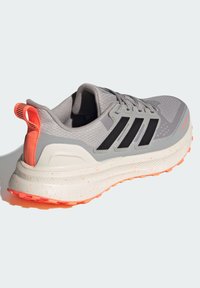 Grå atletisk sko med sorte accenter, tekstureret overdel, orange hælflap, polstret sål med sprækkede hvide detaljer og åndbart design.