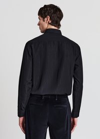 Camicia nera con sottili righe verticali, maniche lunghe e colletto classico, abbinata a pantaloni in velluto blu navy con tasche posteriori.