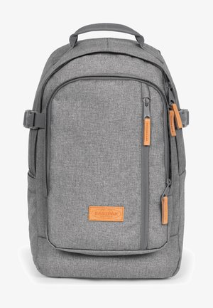 Gray fabric backpack with a textured finish, featuring a tan leather label, zippered pockets, and adjustable straps.