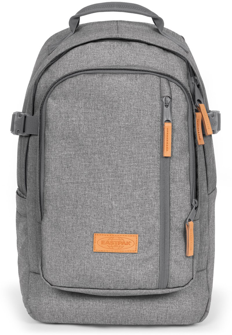Zaino in tessuto grigio con finitura testurizzata, dotato di etichetta in pelle beige, tasche con zip e spallacci regolabili.