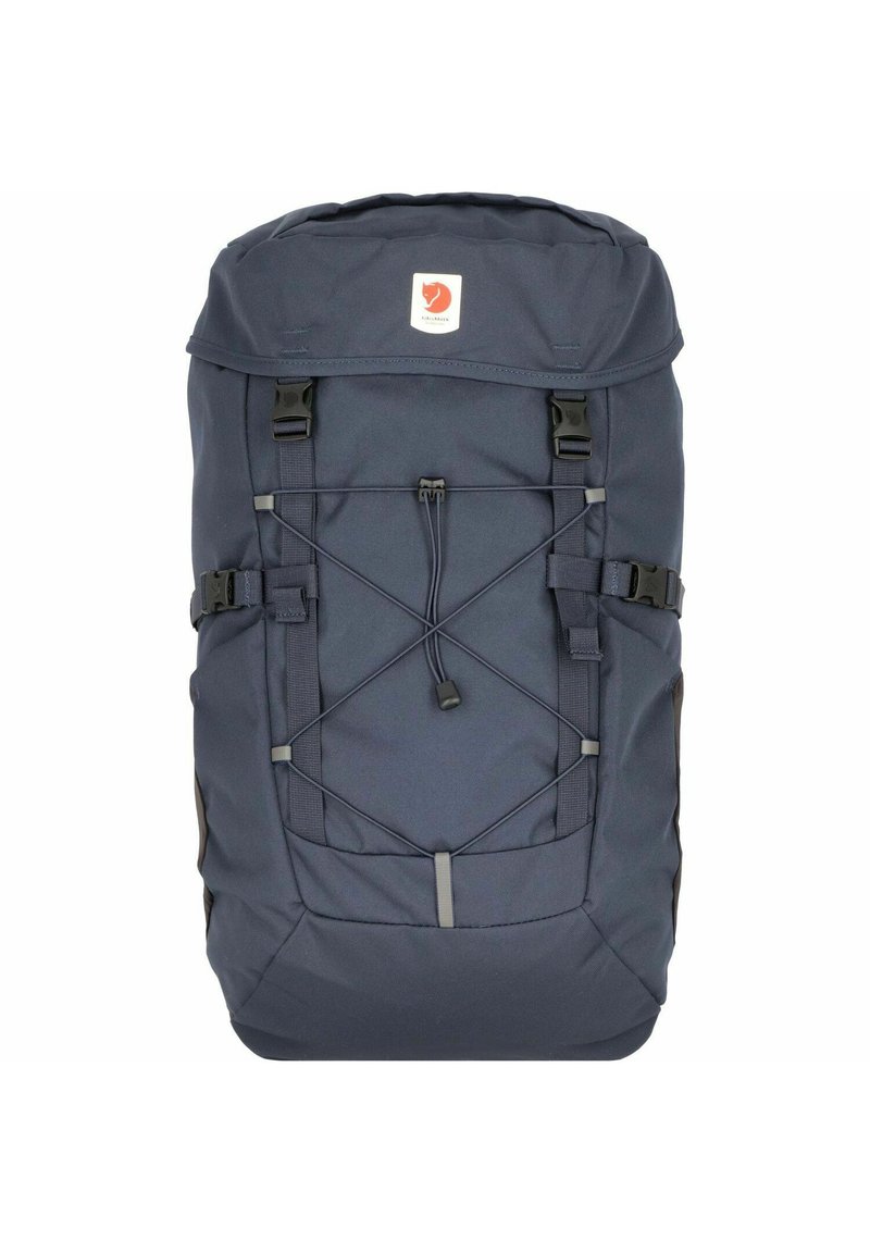 Mochila azul marino con cierre de rollo, cordón elástico frontal, correas ajustables duales y un parche de logo de la marca en la parte frontal.