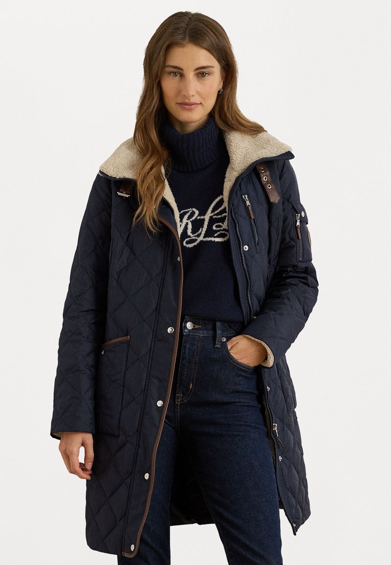 Mornarska jakna od čvrstog materijala s kremastim umjetnim krznom na ovratniku i smešnim kožnim detaljima. Ima džepove sa zipom i kopčama, duge rukave i dizajn do koljena.