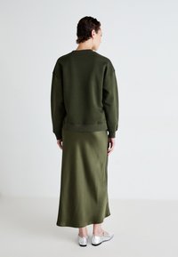 Olívazöld, oversized pulcsi és selyem midi szoknya, ezüst balerinával párosítva. Sima textúra, laza szabás és letisztult dizájn.