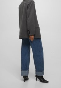 Blazer gris à fines rayures avec une coupe ample, associé à un jean en denim bleu clair retroussé et des escarpins noirs pointus.