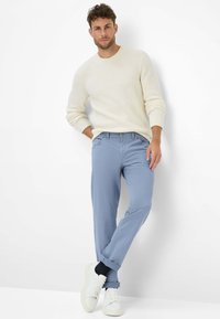 Maglione grigio chiaro a maglia con texture a coste, abbinato a chinos blu chiaro arrotolati. Sneakers bianche completano l'outfit.