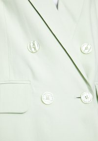 Lysegrøn dobbeltradet blazer med glat tekstur; har to store, gennemsigtige knapper og en brystlomme.