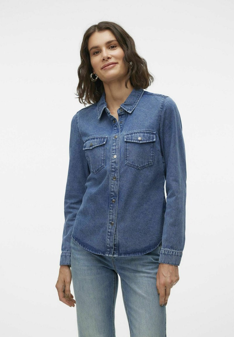 Blaue Jeanshemd mit Knopfleiste, zwei Brusttaschen und langen Ärmeln. Der Stoff hat eine glatte Textur und einen klassischen Kragen.