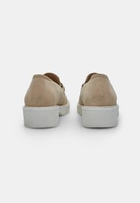 Scarpe in suede beige con suola piatta bianca. Tacchi arrotondati e finitura liscia, con dettagli di cucitura discreti lungo i bordi.