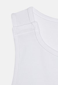 Haut sans manches blanc avec un décolleté rond et des coutures renforcées aux épaules, fabriqué à partir d'un tissu en coton mélangé lisse.