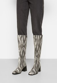 Botas até ao joelho com um padrão em espiral preto e branco, feitas de material suave, com bico fino e salto empilhado.