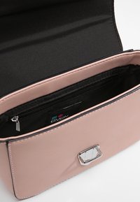 Kompaktní růžová syntetická kabelka se lesklým stříbrným kováním na zapínání, hladkým povrchem a černou textilní podšívkou, vybavená vnitřní kapsou na zip.
