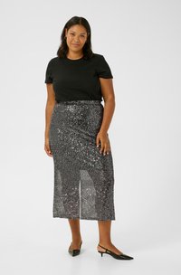 Tricou negru și fustă midi din paiete argintii, cu croială dreaptă. Fusta are o textură strălucitoare și slituri laterale, fiind asortată cu pantofi slingback negri.