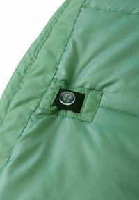 Jasnozielony materiał izolowany, o pikowanej teksturze, z czarną pętlą i przezroczystym guzikiem do zapięcia.