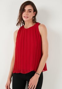 Rød plisseret ærmeløs bluse med rund halsudskæring. Lavet af letvægtsstof, har den et flydende design og falder til en buet kant.