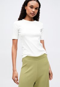 Biała koszulka z krótkim rękawem w dopasowanym kroju. Zestawiona z luźnymi, jasnzielonymi spodniami z prążkowanym pasem. Gładka tekstura.