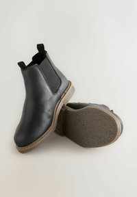 Schwarze Leder-Chelsea-Stiefel mit elastischen Seitenpaneelen, abgerundetem Zehenbereich und strukturierten Sohlen. Mit einer hellbraunen Kante um die Sohle.