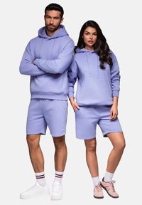Des sweatshirts et des shorts violet clair, fabriqués en tissu doux. L'homme porte un sweatshirt et des shorts avec une poche ; la femme a un sweatshirt et des shorts à coupe décontractée.