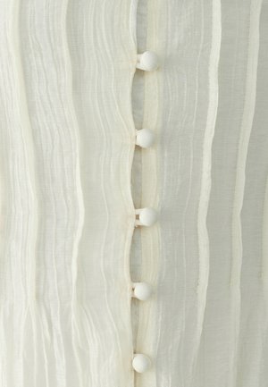 Detailný záber bielej priehľadnej látky s vertikálnou vlnitou štruktúrou a radom piatich gombíkov pokrytých látkou v strede.