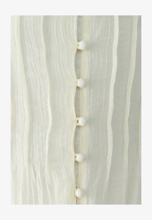 Gros plan sur un tissu blanc transparent avec une texture ondulée verticale et une rangée de cinq boutons recouverts de tissu au centre.