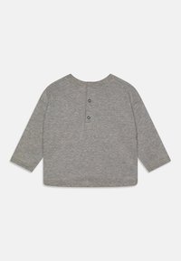 Chemise grise à manches longues en tissu doux, avec un col arrondi et une fermeture par deux boutons à l'arrière. Texture simple et lisse.
