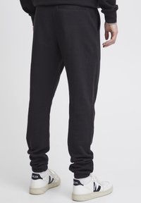 Schwarze Sweatpants mit weicher Textur, elastischen Bündchen und einer rückseitigen Taschenpartie, kombiniert mit weißen Sneakers mit schwarzen Akzenten.
